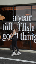 Person standing on a street with a reflection of a store front in the glass.