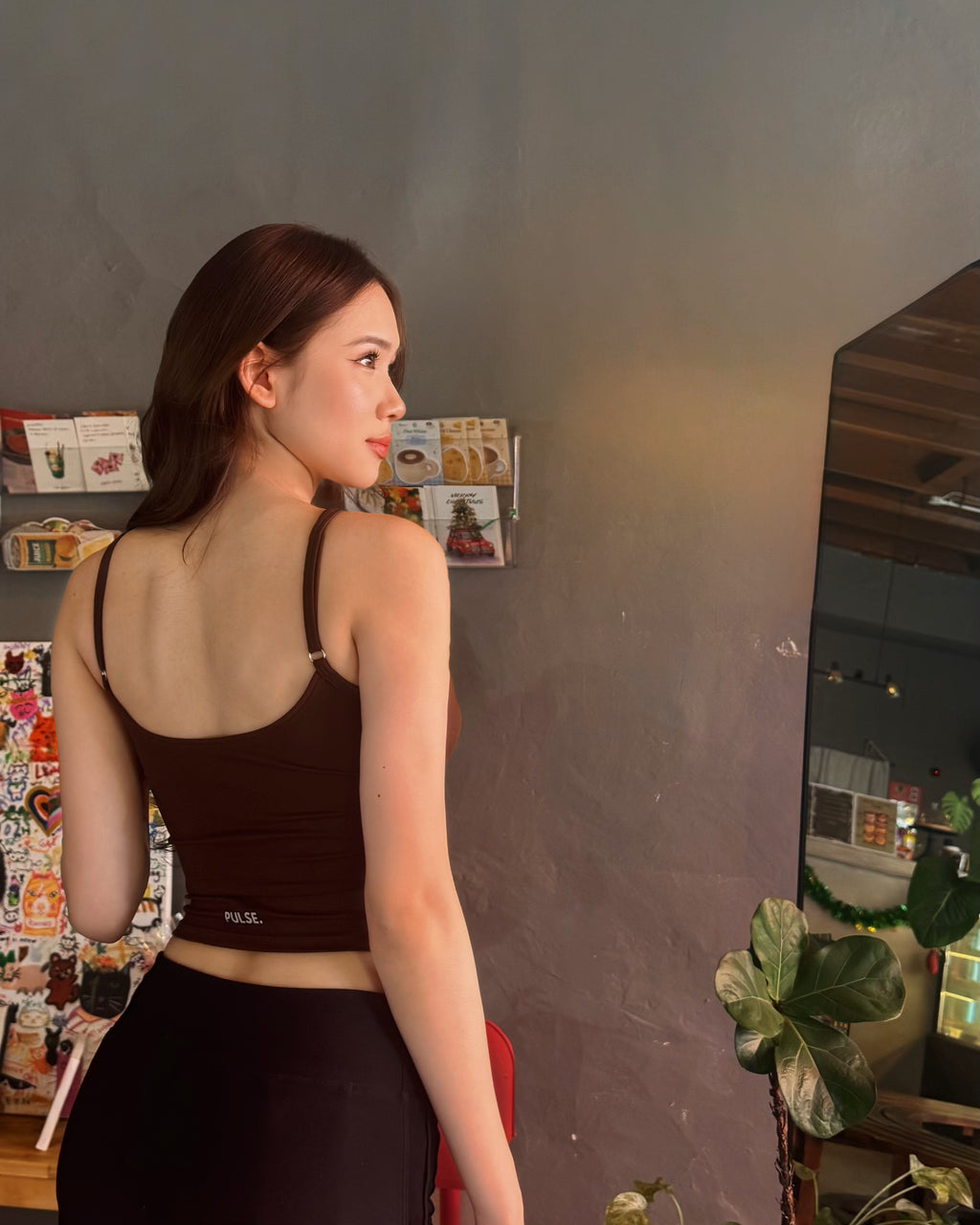 Woman wearing a black sports bra and leggings in a room with a gray wall and plants.
