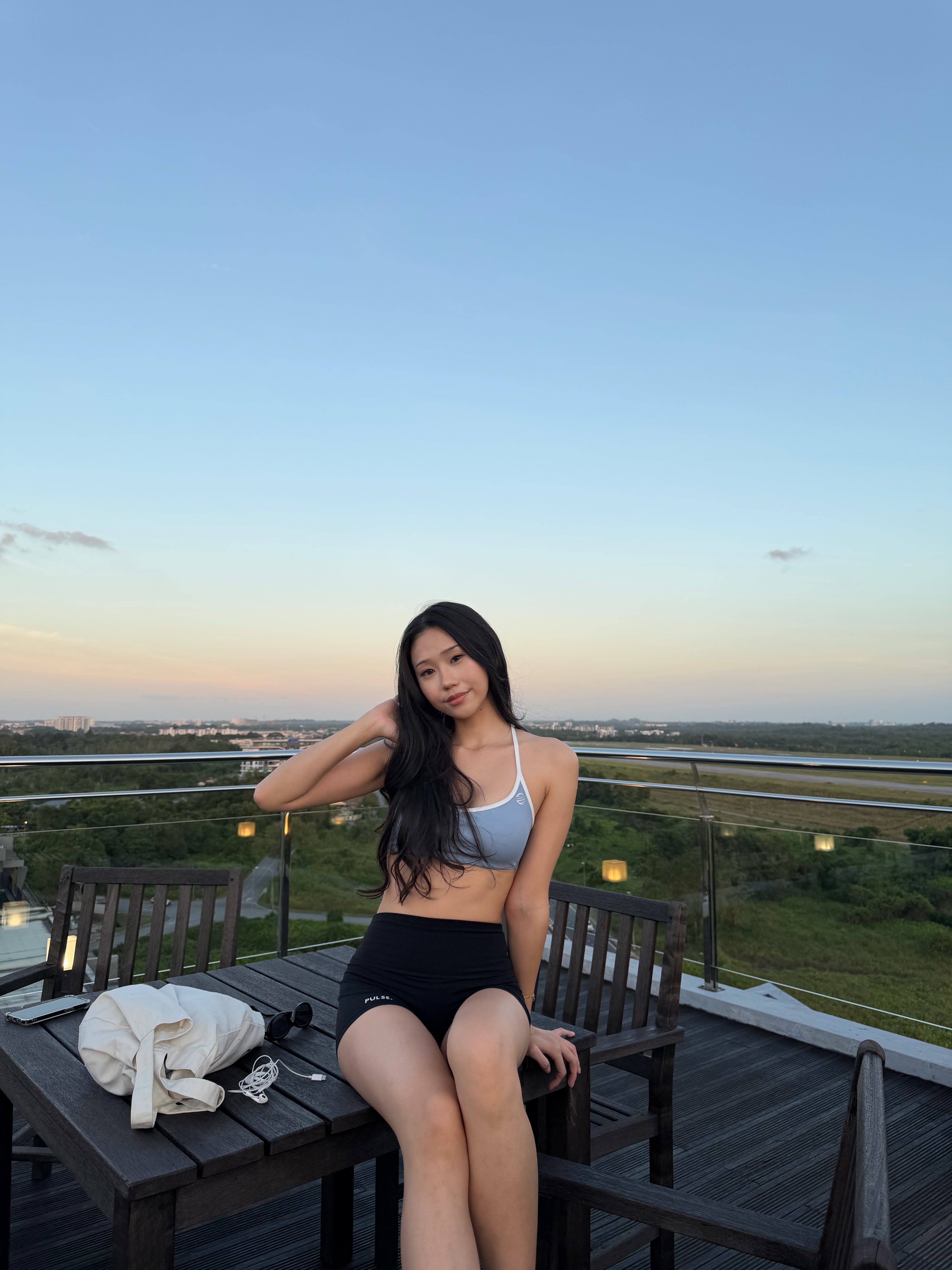 Woman sitting on a rooftop deck with a scenic view at sunset.