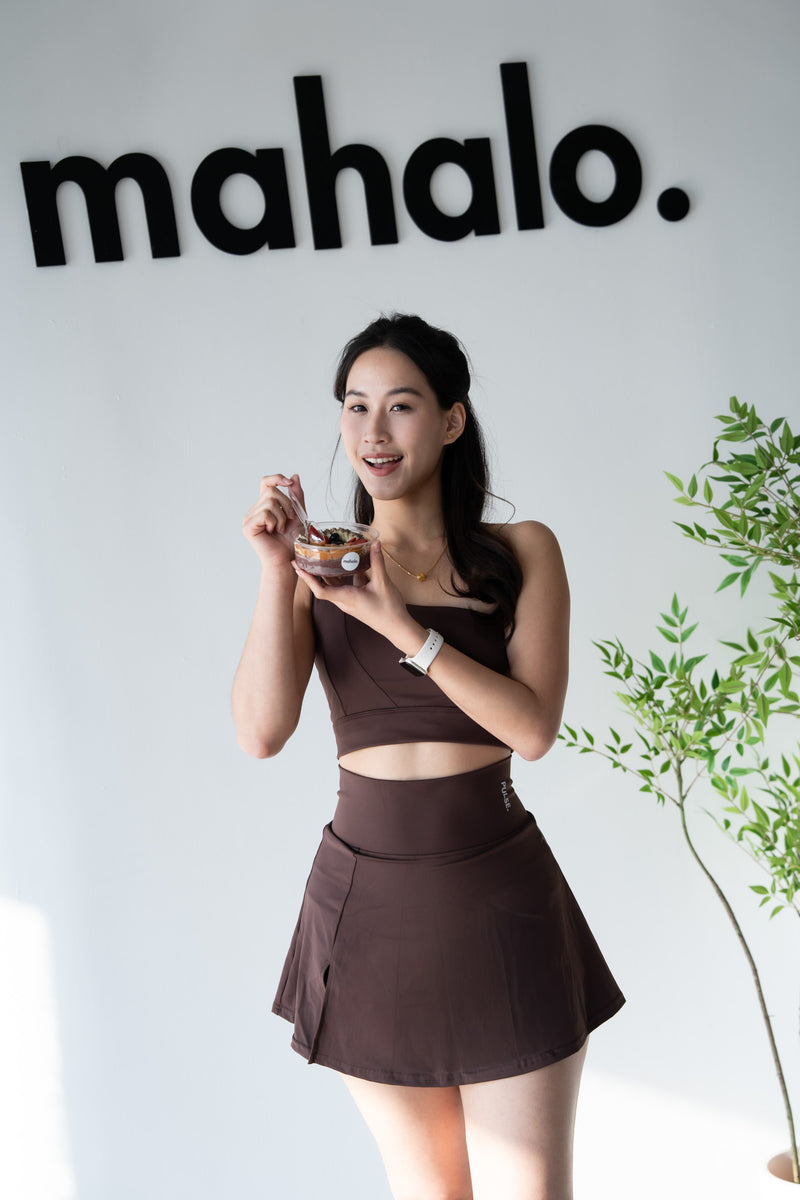Woman in a brown outfit holding a drink with 'mahalo.' branding in the background